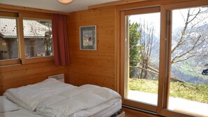 Ein Zimmer in einer Holzhütte mit einem Bett, einem Fenster mit Bergblick und einem Bild in einem Rahmen an der Wand.