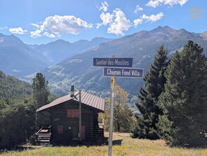 Une cabane en bois, sur laquelle est apposée une pancarte indiquant « Sentier des Moulins » et « Chemin Fond Villa », dans une zone montagneuse.