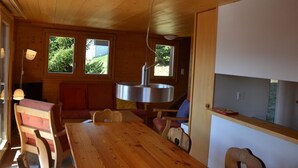 Ein Holzblockhaus-Innenraum mit Esstisch, Bänken und einem großen Fenster mit Blick auf Grünflächen.