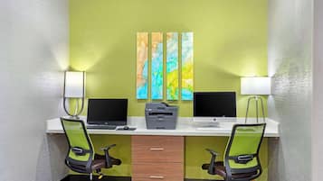 Un espace de travail comprenant deux bureaux, chacun équipé d’un écran d’ordinateur, d’un clavier et d’une imprimante. On y trouve également deux chaises de bureau, un bureau blanc et une lampe fixée au mur.