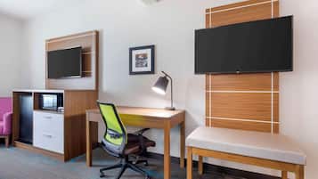 Ein Hotelzimmer mit Schreibtisch aus Holz, einem Sessel, einem an der Wand montierten Fernseher, einer kleinen Kommode und einem gerahmten Bild.