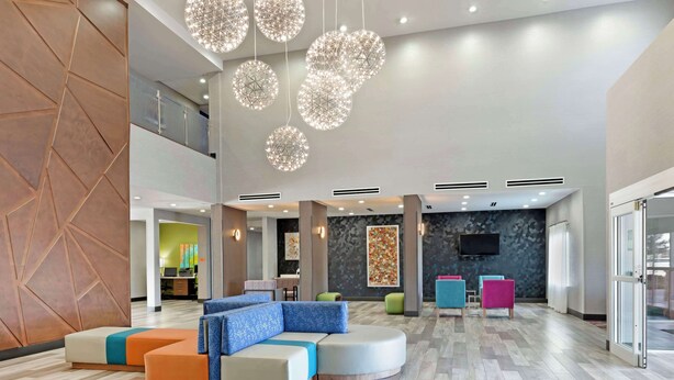 Eine großzügige Lobby mit modernem Design, ausgestattet mit einer Sitzecke mit bunten Kissen, einer großen Chandelieber und einem an der Wand befestigten Flachbildfernseher.