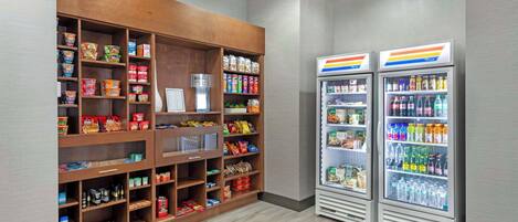Un área de venta automática con opciones de comida y bebida, que incluye una sección refrigerada para bebidas y un estante con diferentes aperitivos.