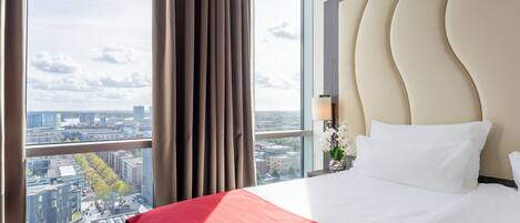 Habitación de hotel con una cama grande, vistas a la ciudad y una ventana con cortinas.