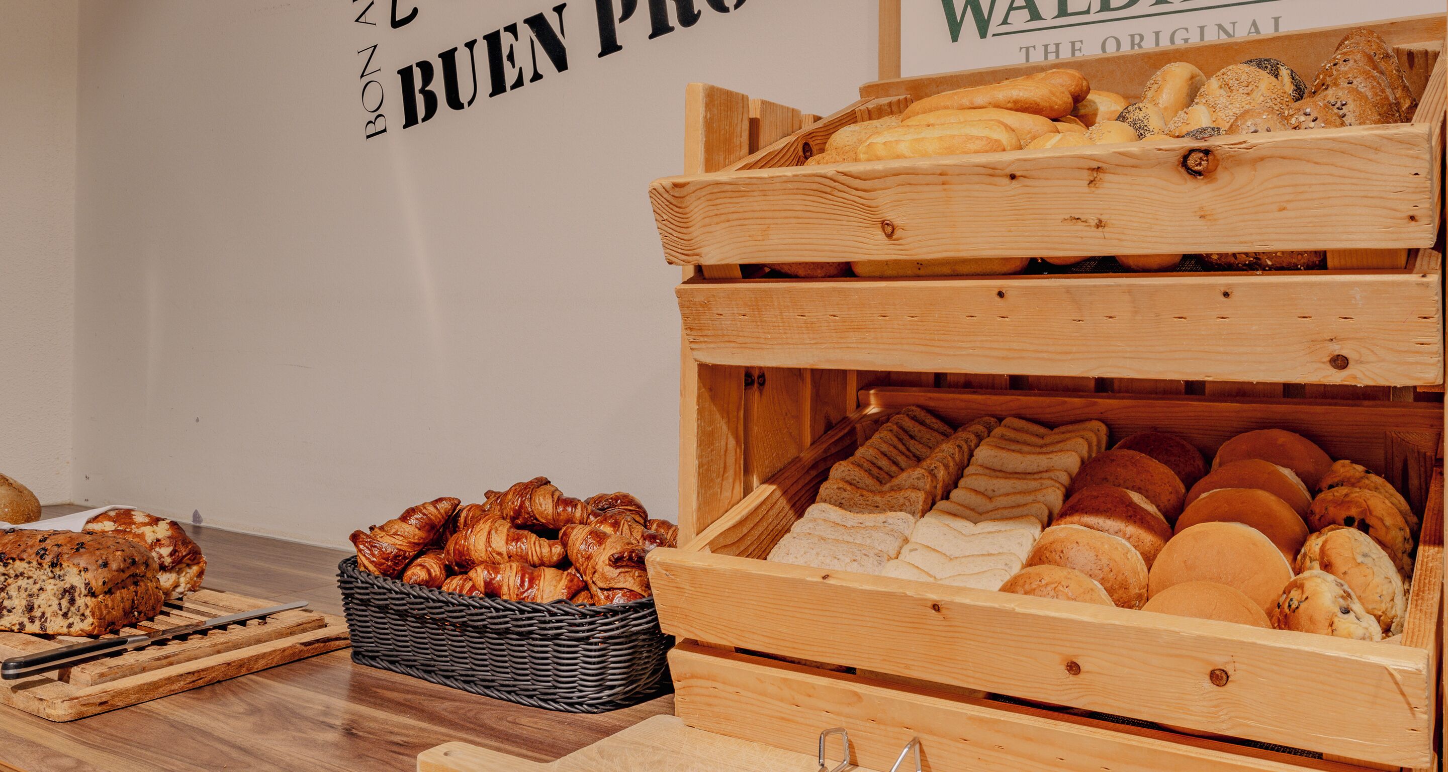 Una exhibición de panadería con diversos panes y pasteles en cajas y cestas de madera.