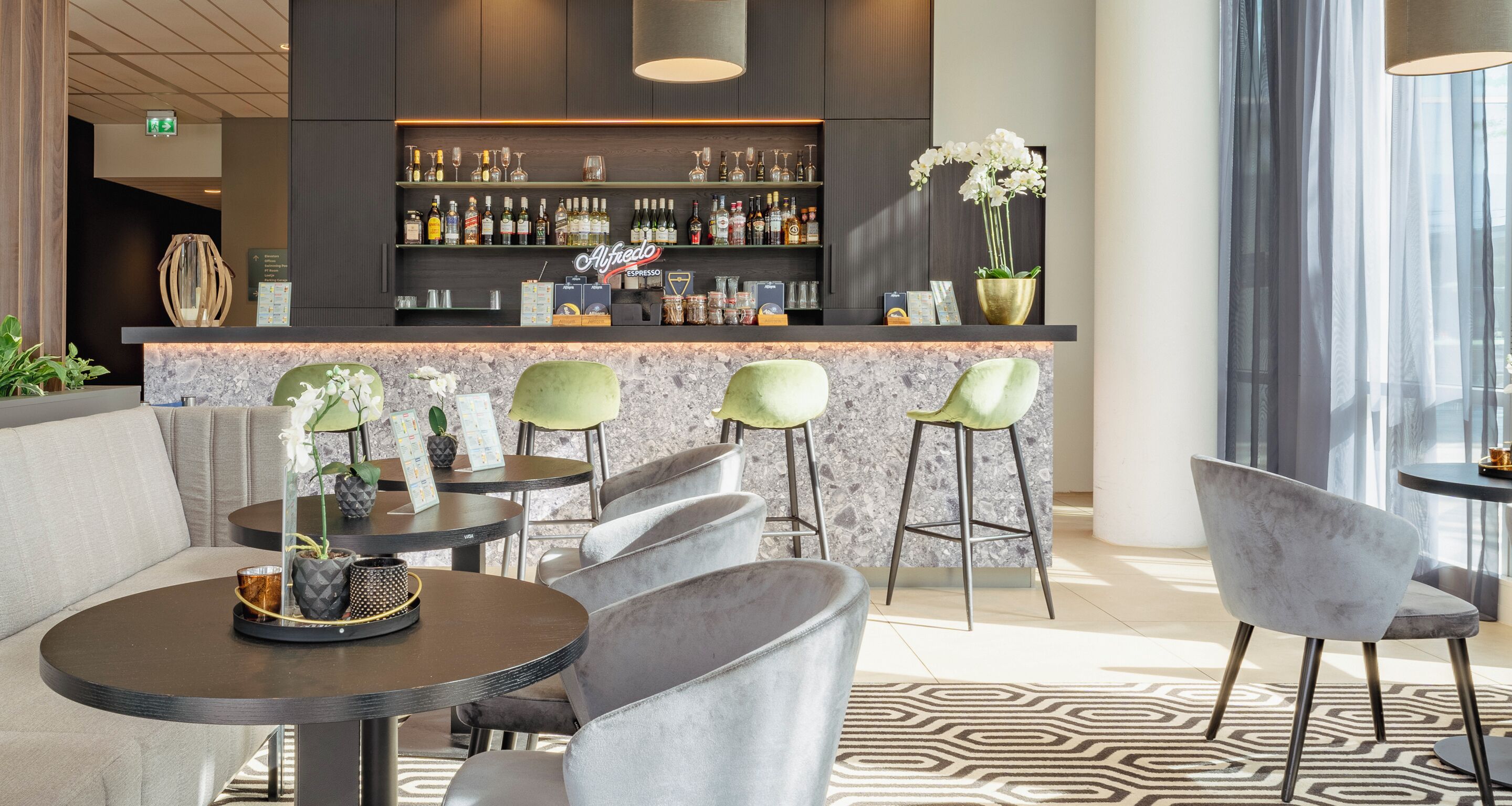 Un área de bar moderna con mostrador de mármol, taburetes y una variedad de botellas de licor.