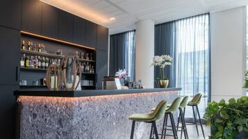 Een moderne bar met een marmeren aanrecht, barkrukken en een verscheidenheid aan flessen en glazen.