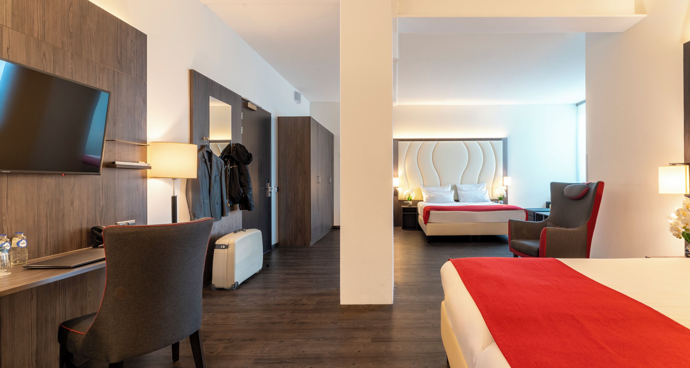 A hotel room with a bed, a desk with a chair, a TV, and a wardrobe.