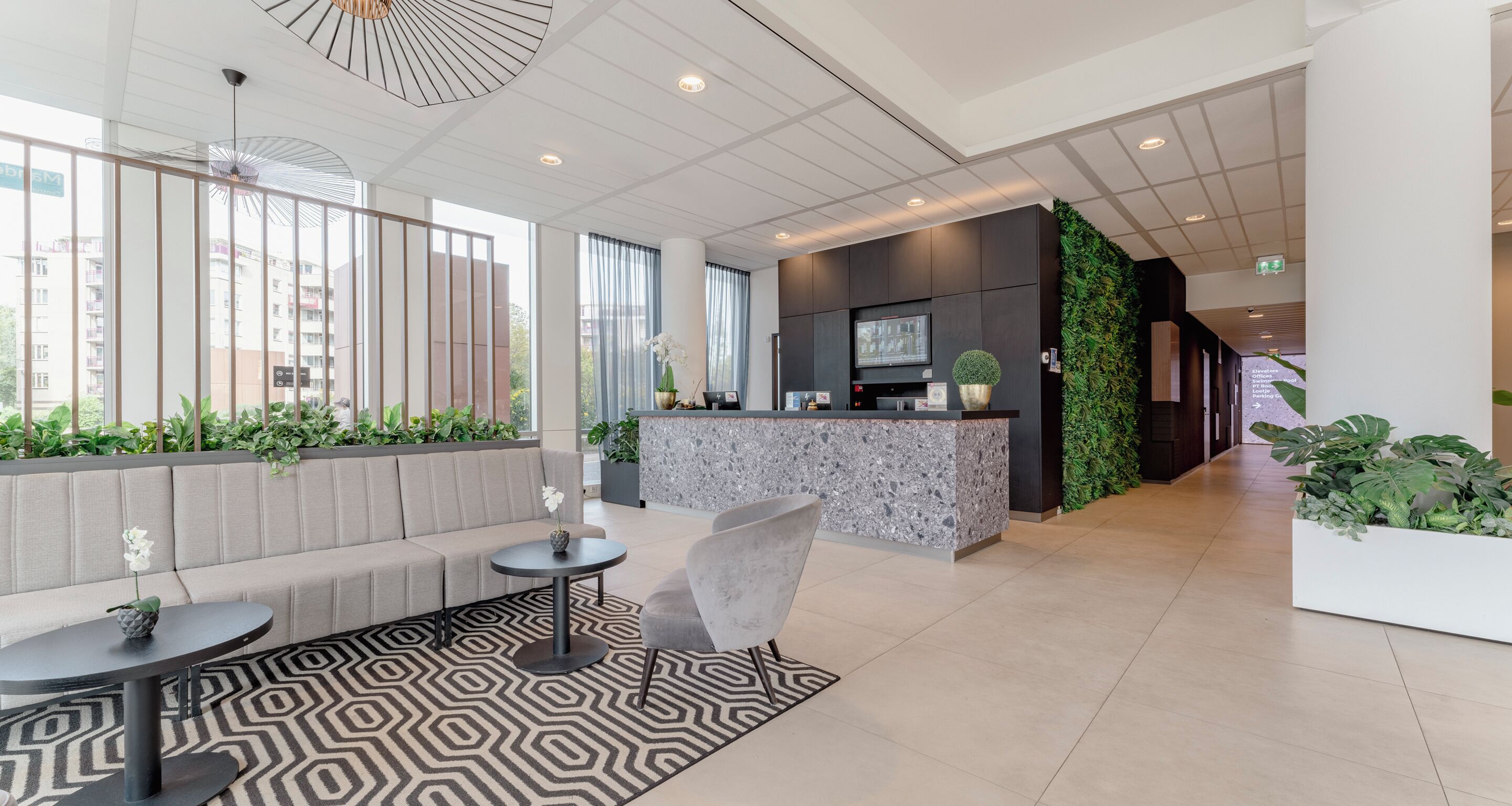 A modern lobby with a reception desk, seating area, and a large window with a view of buildings.