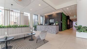 A modern lobby with a reception desk, seating area, and a large window with a view of buildings.
