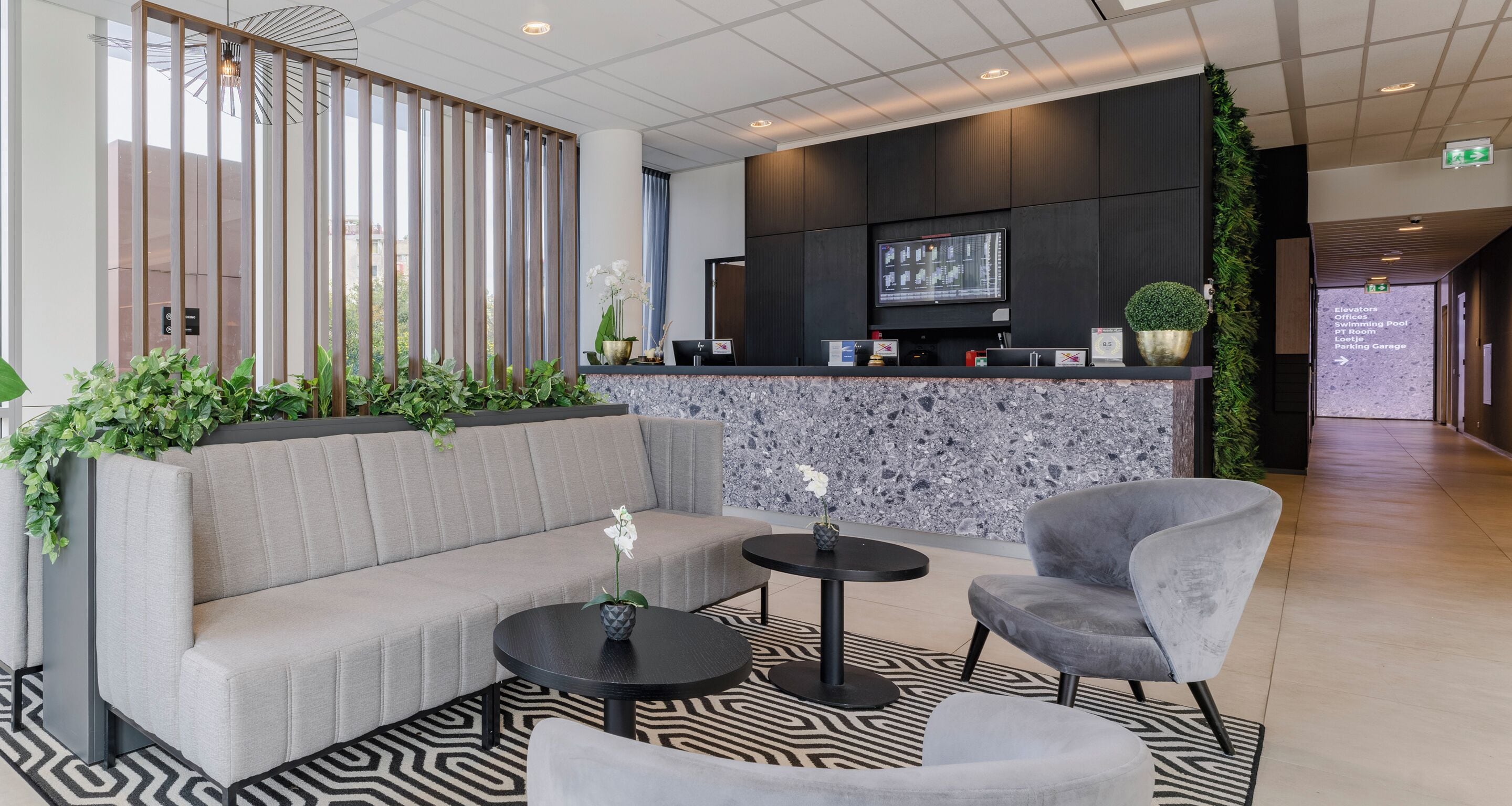 A modern lobby with a reception desk, seating area, and a large screen displaying information.