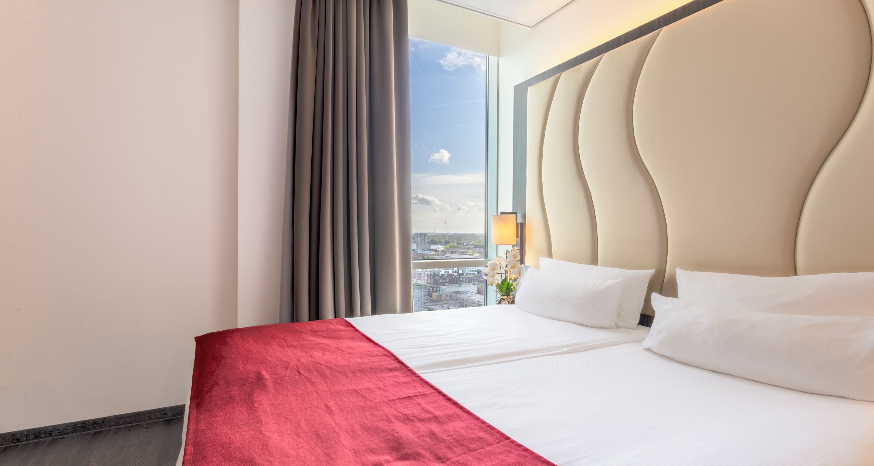 A hotel room with a large bed, a view of the city, and a modern headboard.