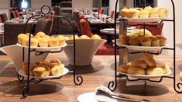A buffet table with multiple trays of muffins and pastries.