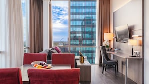 A hotel room with a dining area, a sofa, a desk, and a large window with a city view. - PLAZA Premium Almere (Almere)