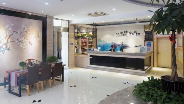 A reception area with a counter, a seating area with a table and chairs, and a wall with a floral mural. - Mengpei Business Hotel (Shaoxing)