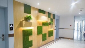A modern reception area with a wooden wall and green accents, a potted plant, and a sign indicating the location. - Mengpei Business Hotel (Shaoxing)