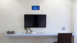 A room with a mounted TV on the wall, a small table with a tissue box, a vase with a plant, and a chair. - Mengpei Business Hotel (Shaoxing)