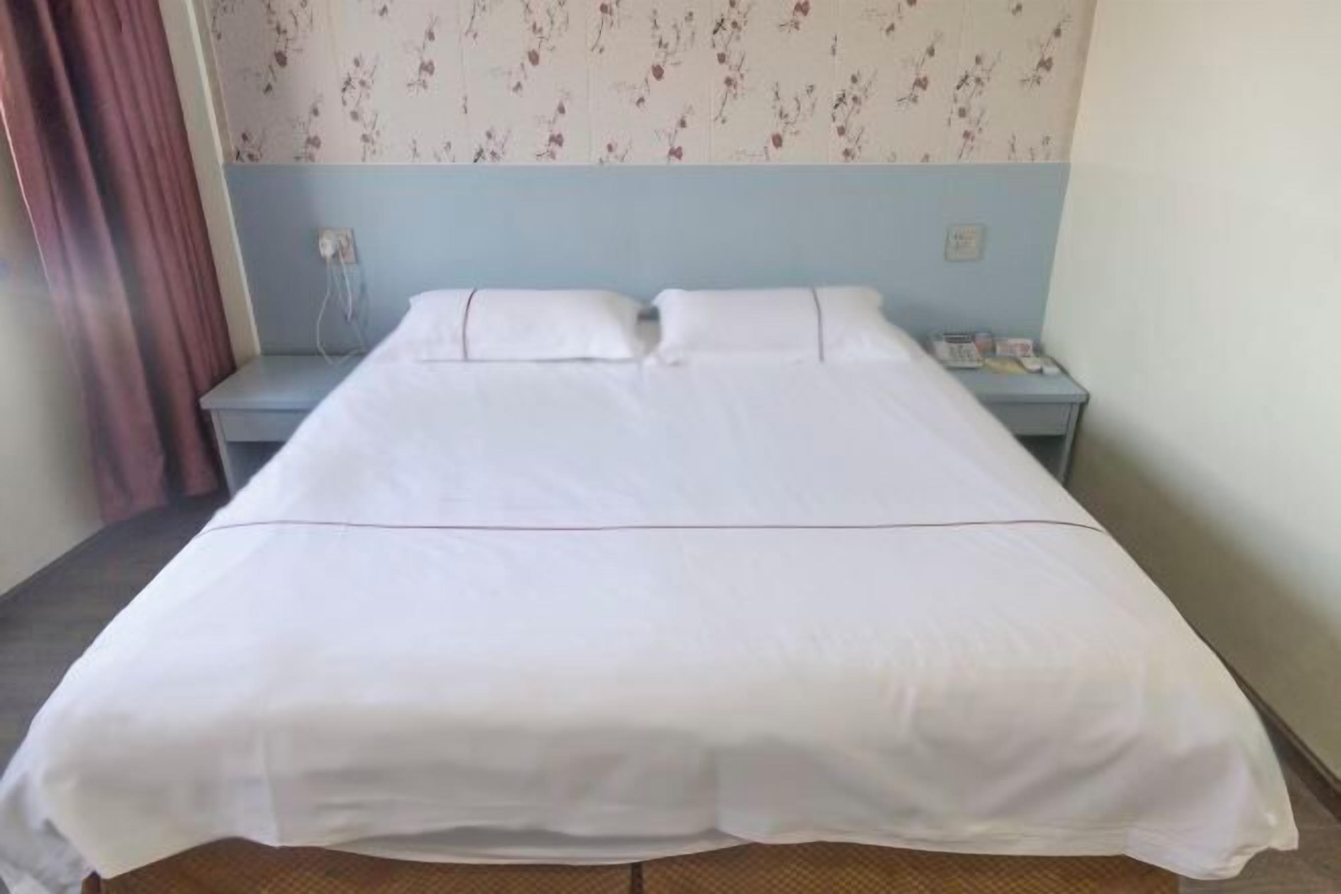 A neatly made bed with white linens in a room with floral wallpaper and a blue accent wall.