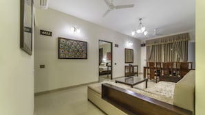 A modern living room with a sofa, coffee table, and dining set. There are wall-mounted lights and a ceiling fan. - Zade House Jaipur (Jaipur)