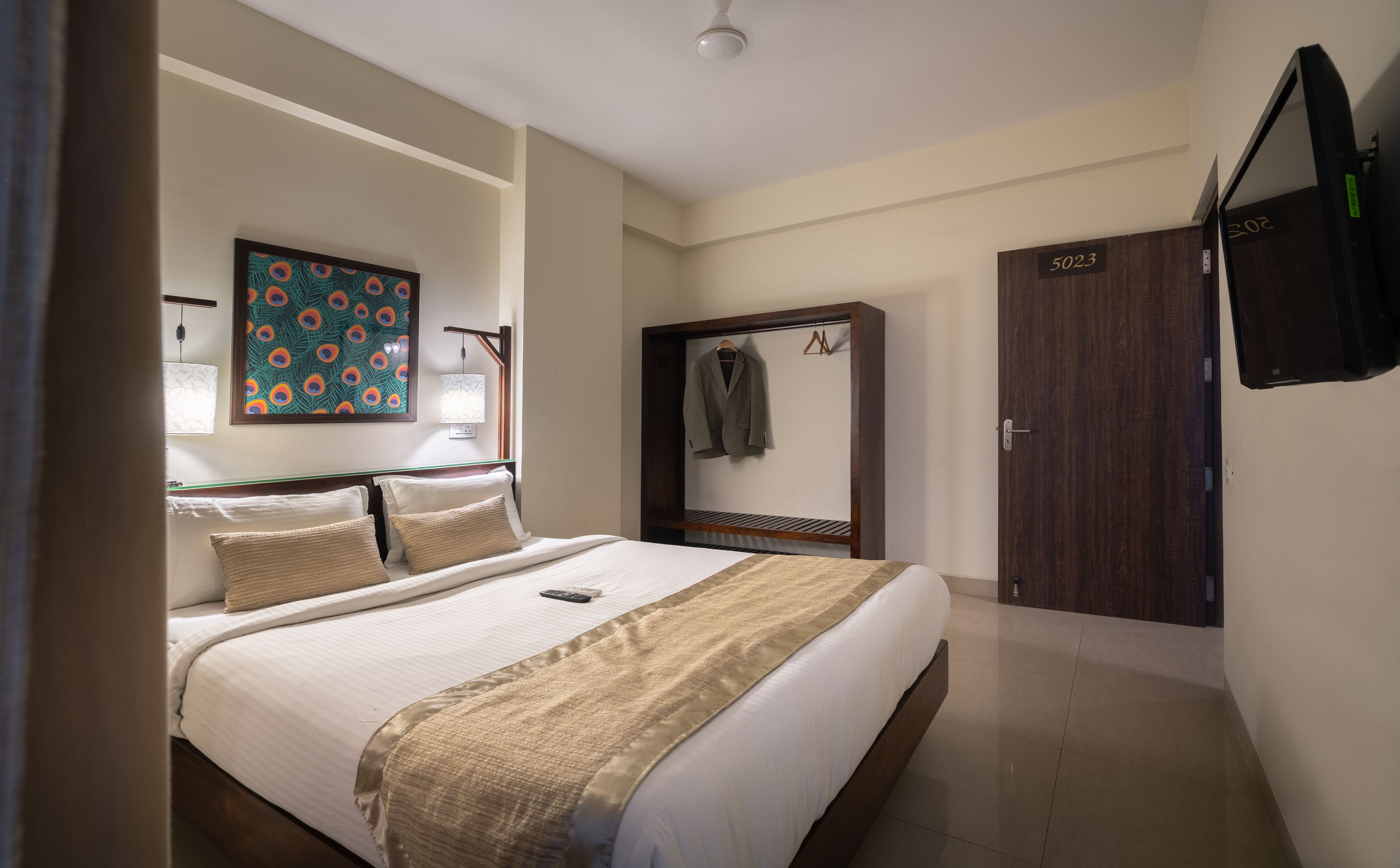 A hotel room with a bed, a wardrobe, a mirror, a painting, and a lamp.