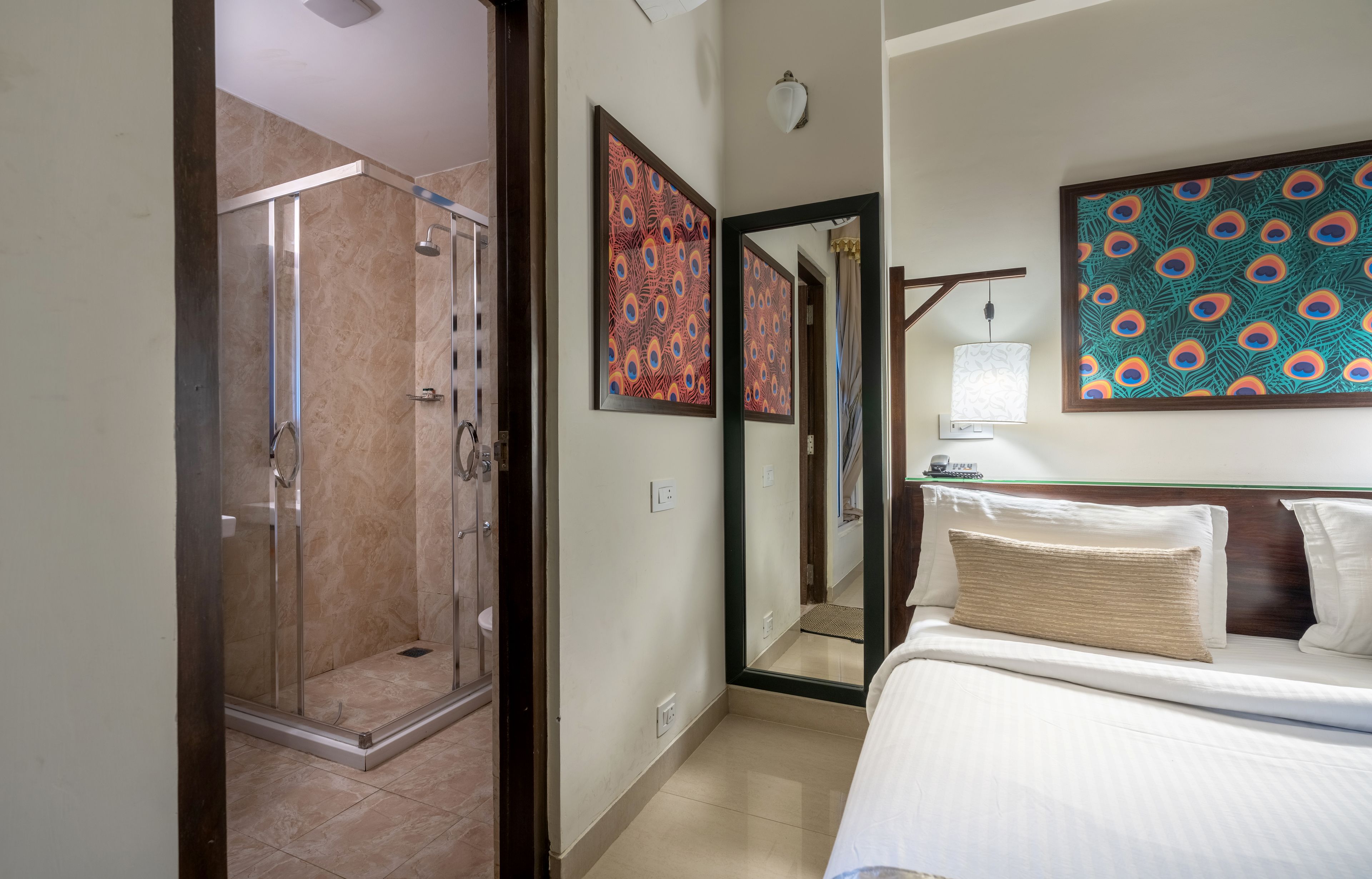 A hotel room with a glass-enclosed shower, a bed with white linens, and two decorative wall art pieces.