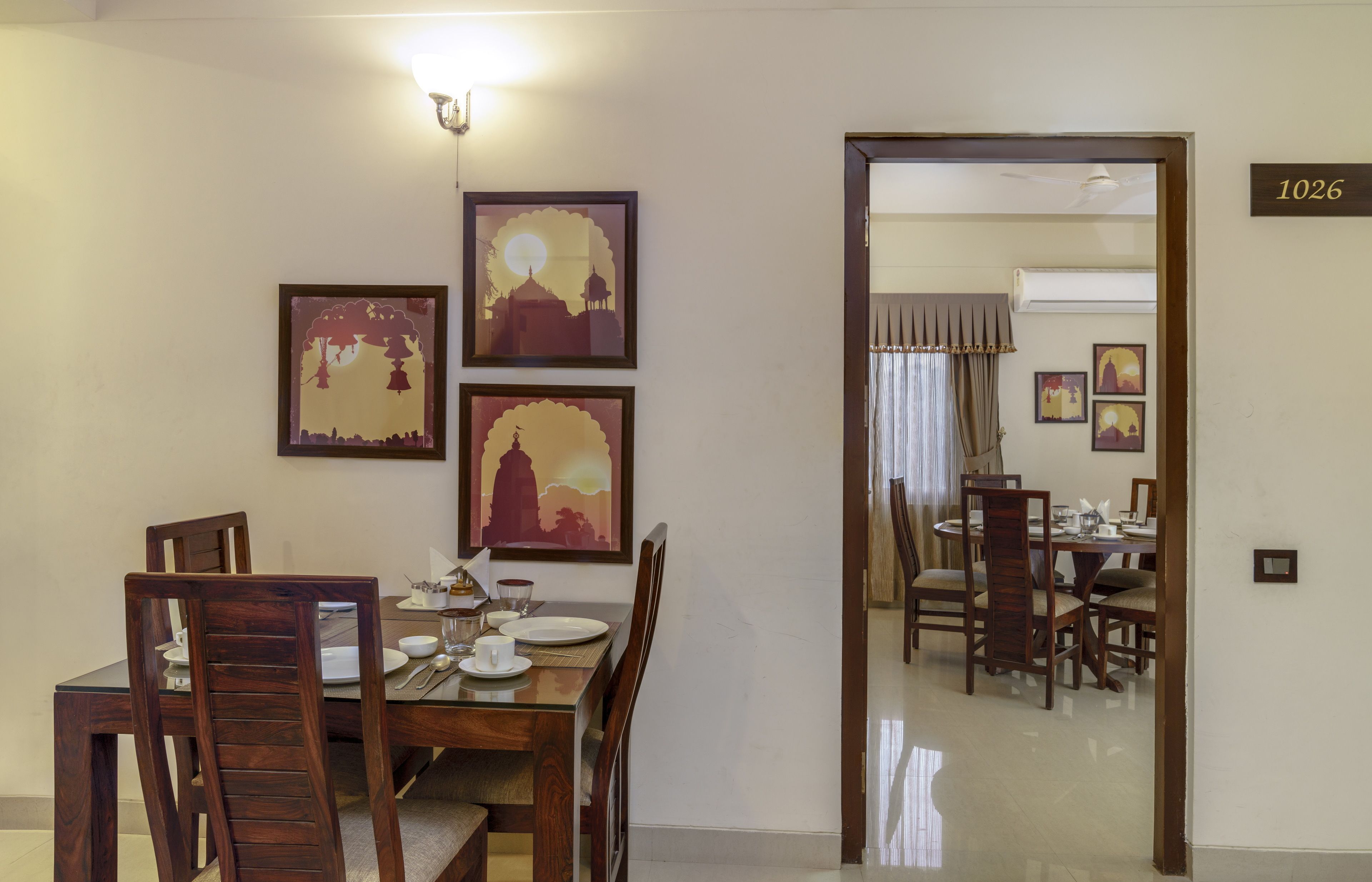 A dining area with a wooden table set for four, framed artwork on the wall, and a number '1026' sign.