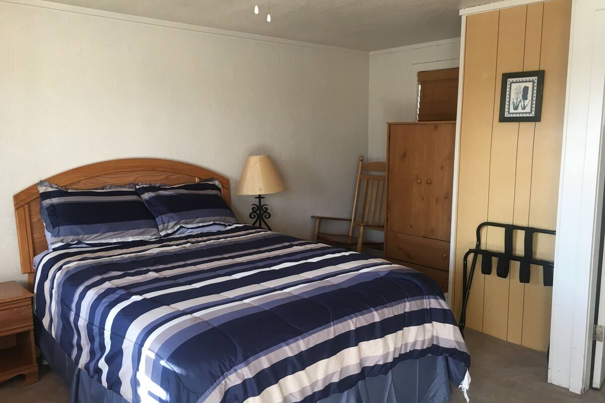 A bedroom with a bed, a wooden headboard, a nightstand, a lamp, a chair, a wardrobe, and a coat rack.