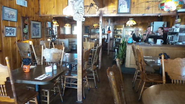 A restaurant with wooden walls and tables, featuring a variety of chairs and a bar area. - Tyee Restaurant and Hotel (Coupeville)