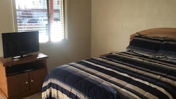 A bedroom with a bed, a TV on a wooden stand, and a window with blinds.