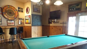 A pool table with a green felt surface, surrounded by wooden paneling and black chairs. - Tyee Restaurant and Hotel (Coupeville)