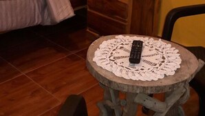 Un dormitorio con una cama, una mesita de noche de madera, una mesa redonda con un control remoto y una silla.