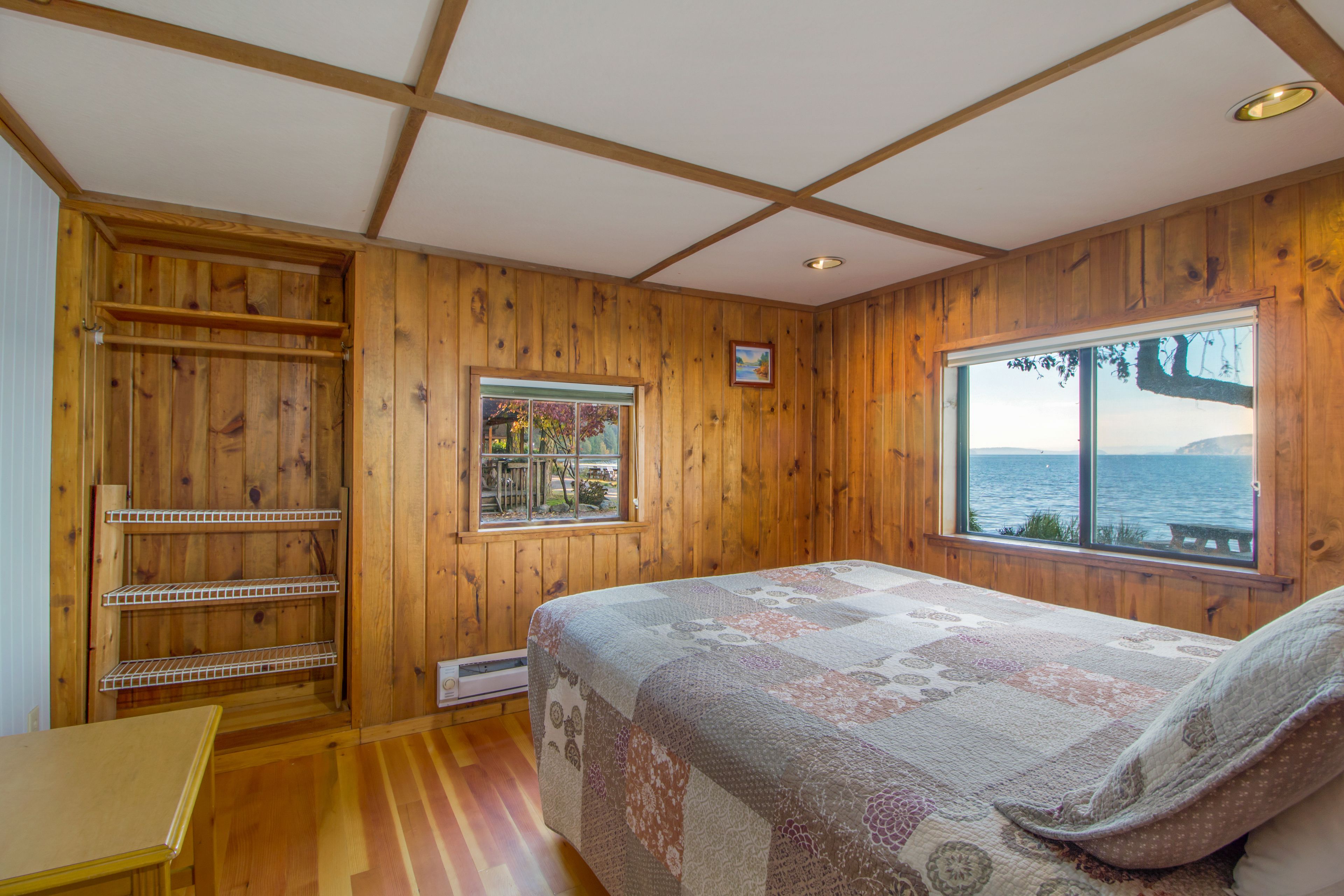 Una habitación con paneles de madera, una cama, una ventana con vistas al mar y una estantería.