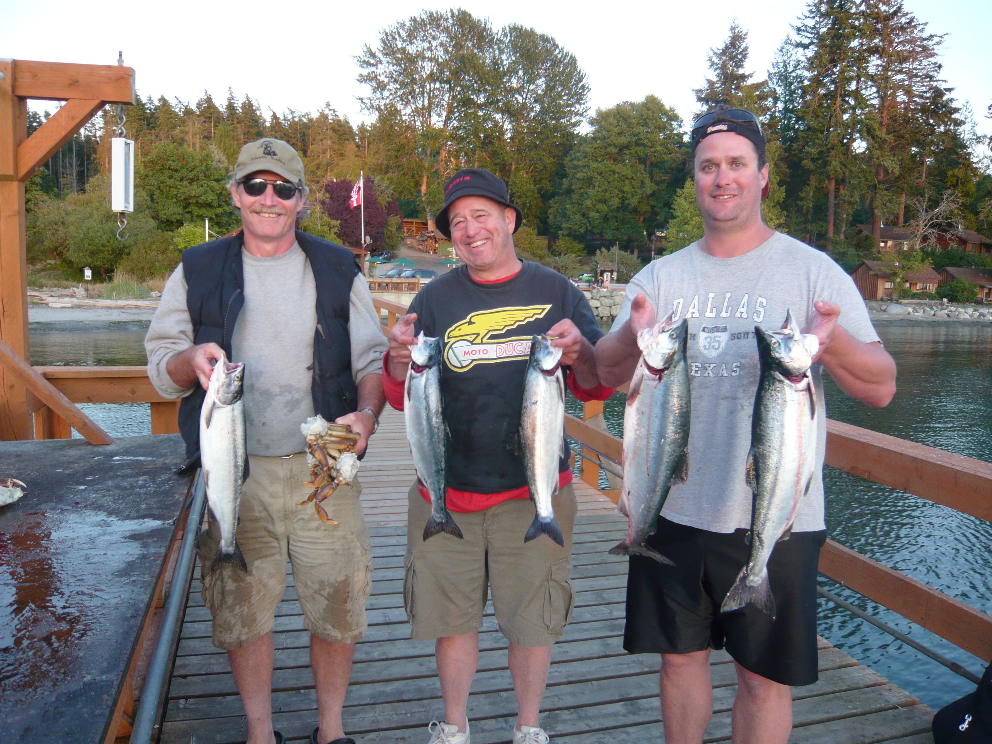 Three people on a wooden dock holding fish.