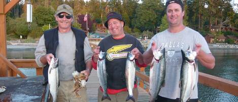 Three people on a wooden dock holding fish.