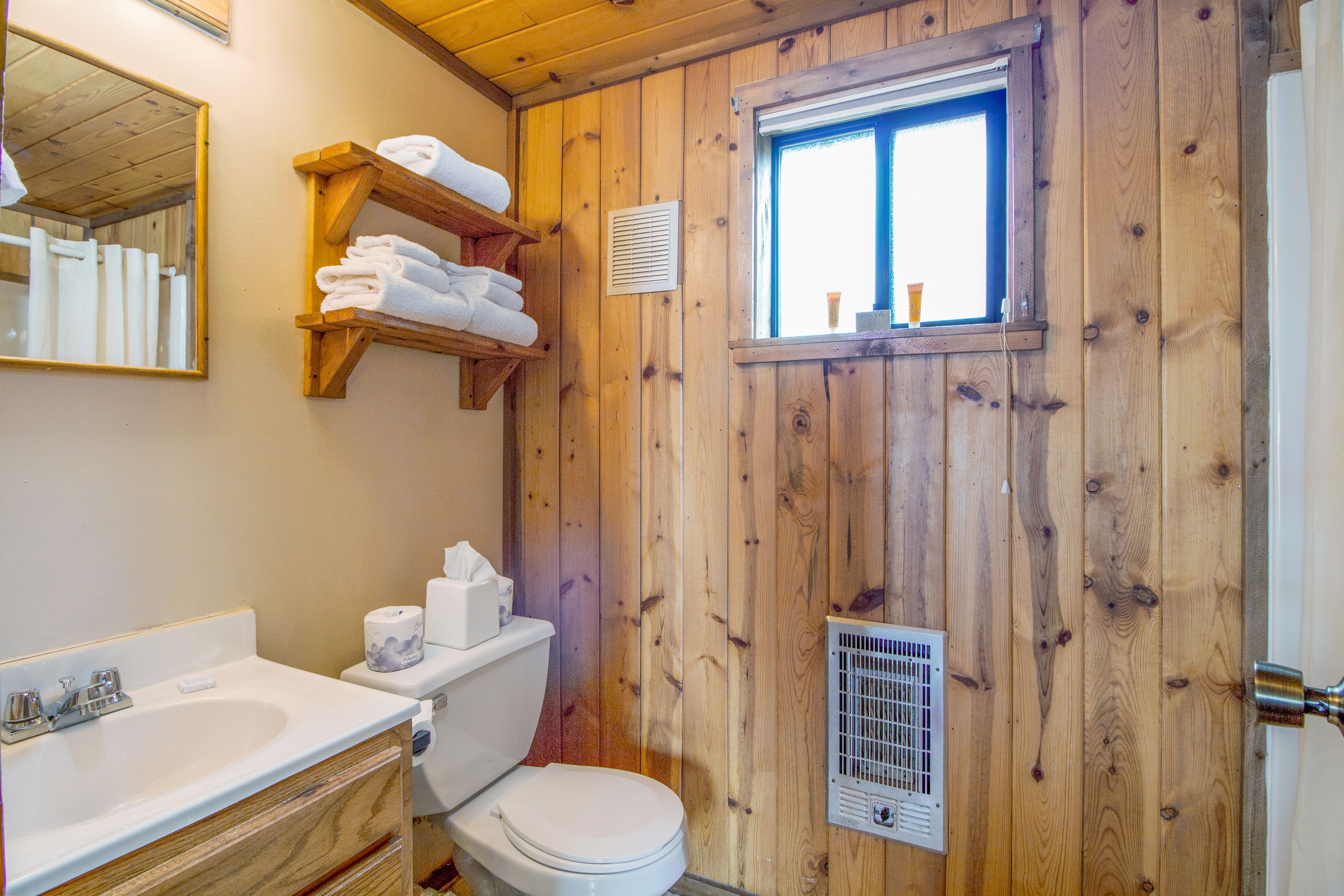 Une salle de bain aux murs lambrissés, équipée de toilettes, d’un lavabo et d’un porte-serviettes.