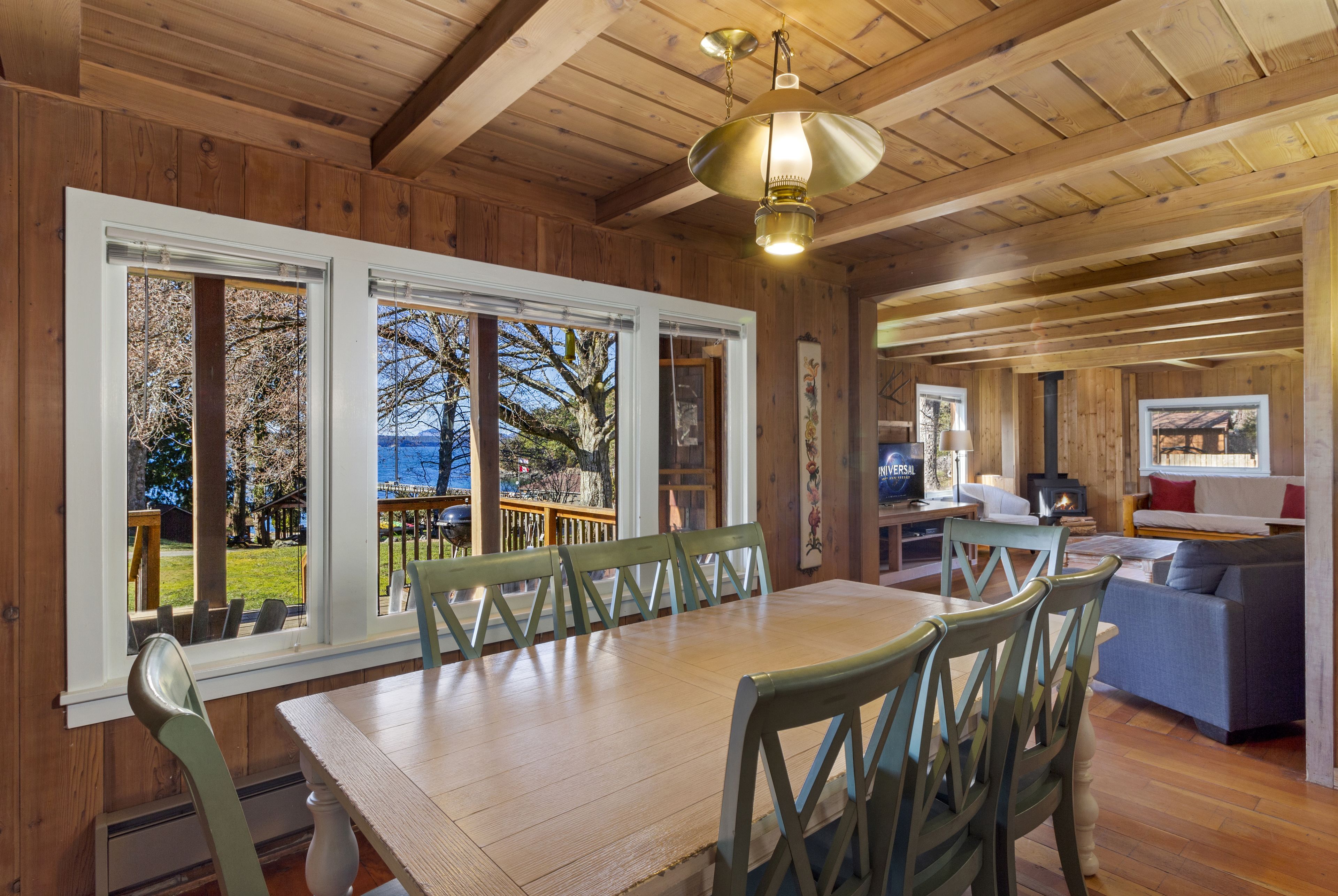 A wooden interior with a dining area, large windows, and a cozy seating area.