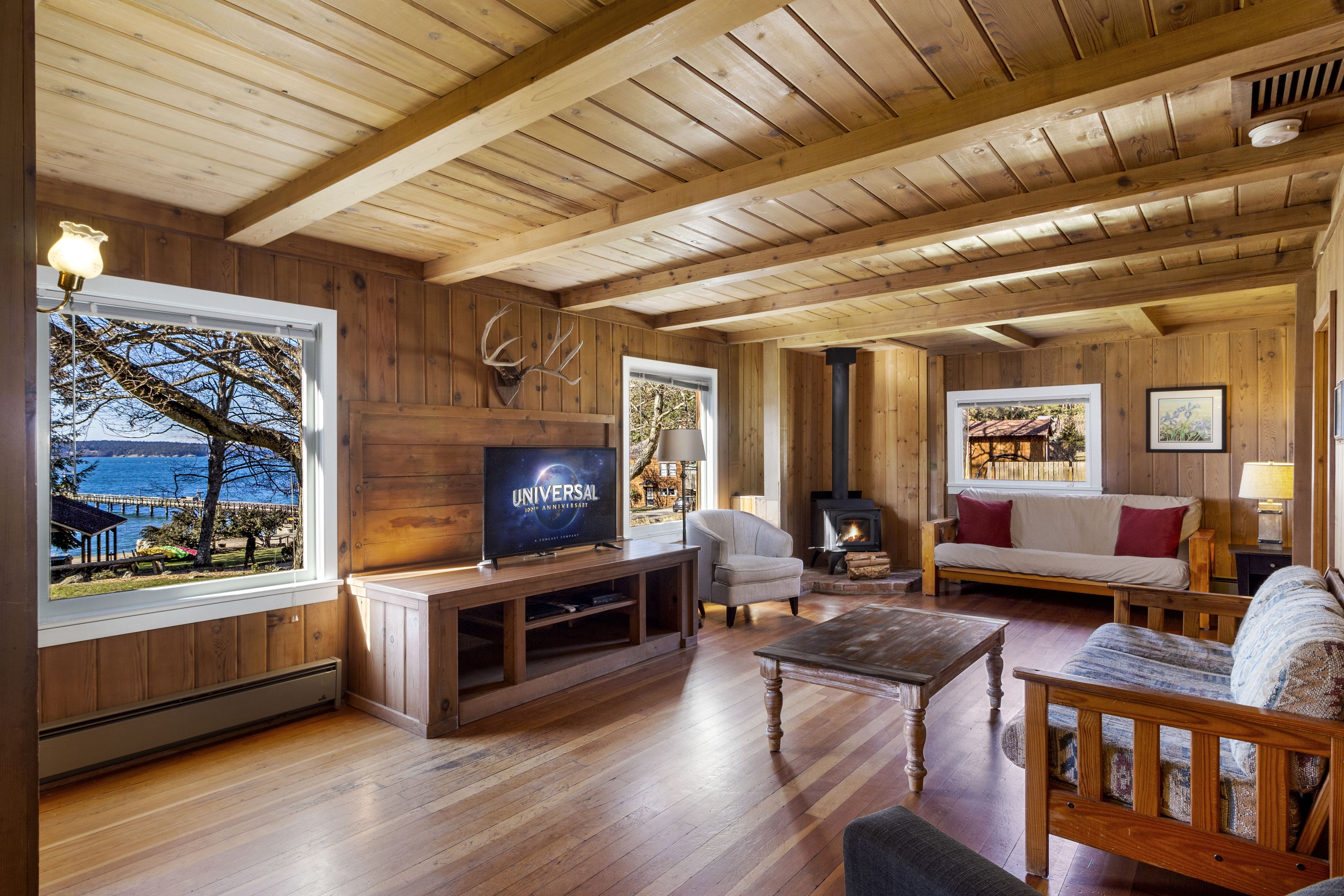 Ambiente interno in legno con televisione, angolo salotto, camino e ampie finestre su una vista panoramica.