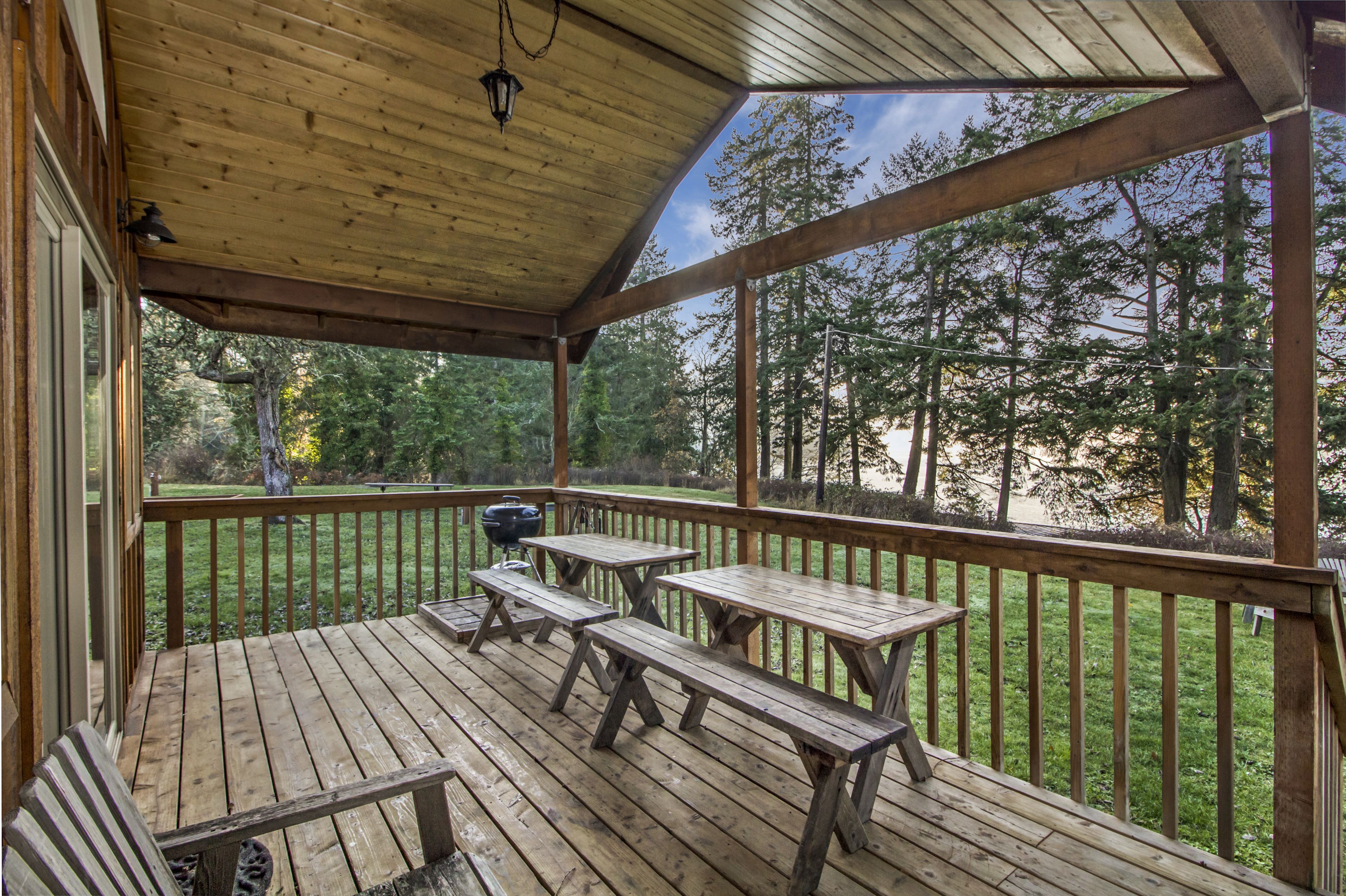 Eine Holzterrasse mit Picknicktischen und einem Grill, mit Blick auf eine bewaldete Landschaft.