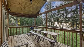 Eine Holzterrasse mit Picknicktischen und einem Grill, mit Blick auf eine bewaldete Landschaft.