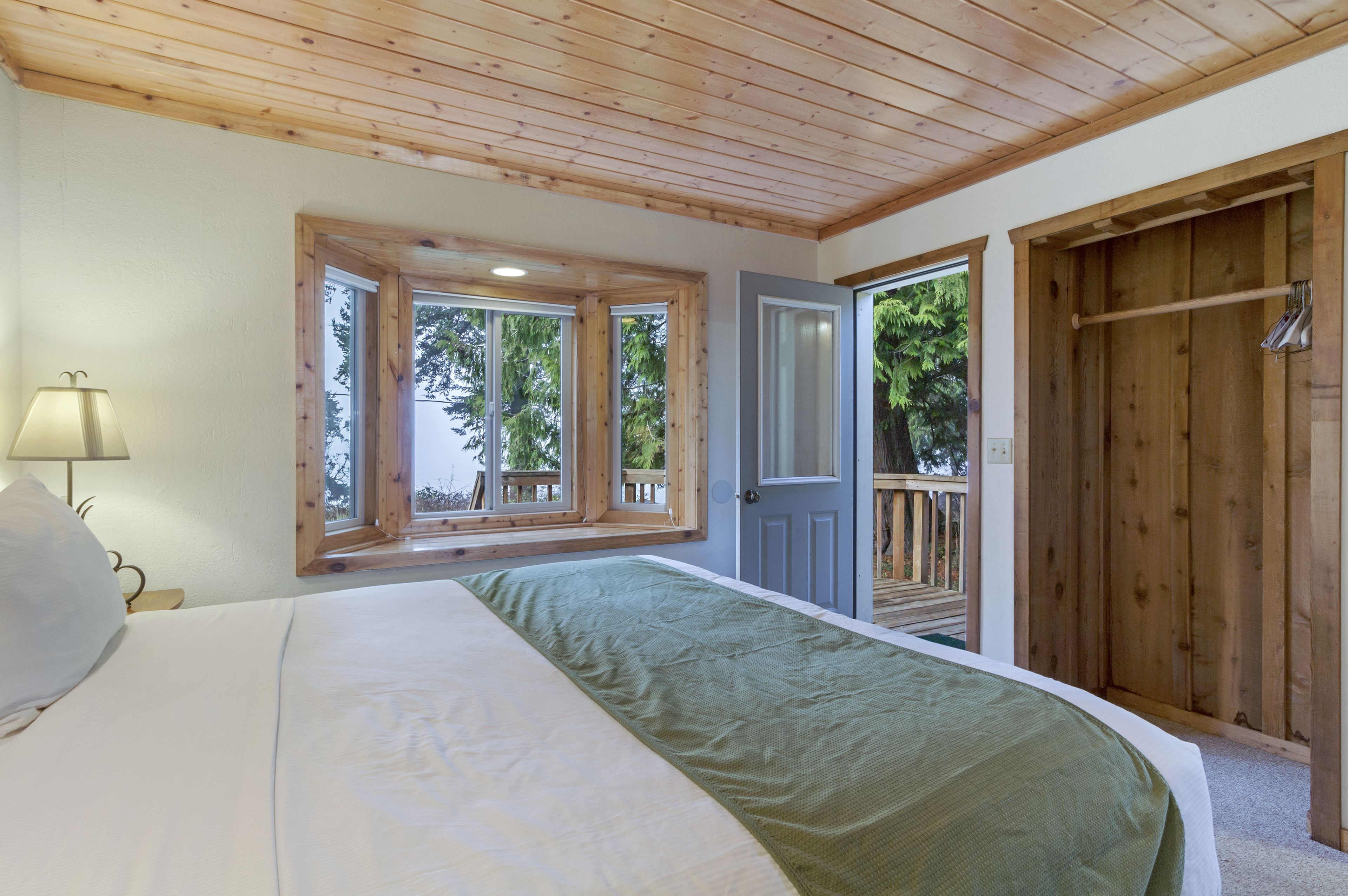 Un dormitorio con techo de madera, una cama con manta verde, una ventana y una puerta que da a una terraza exterior.