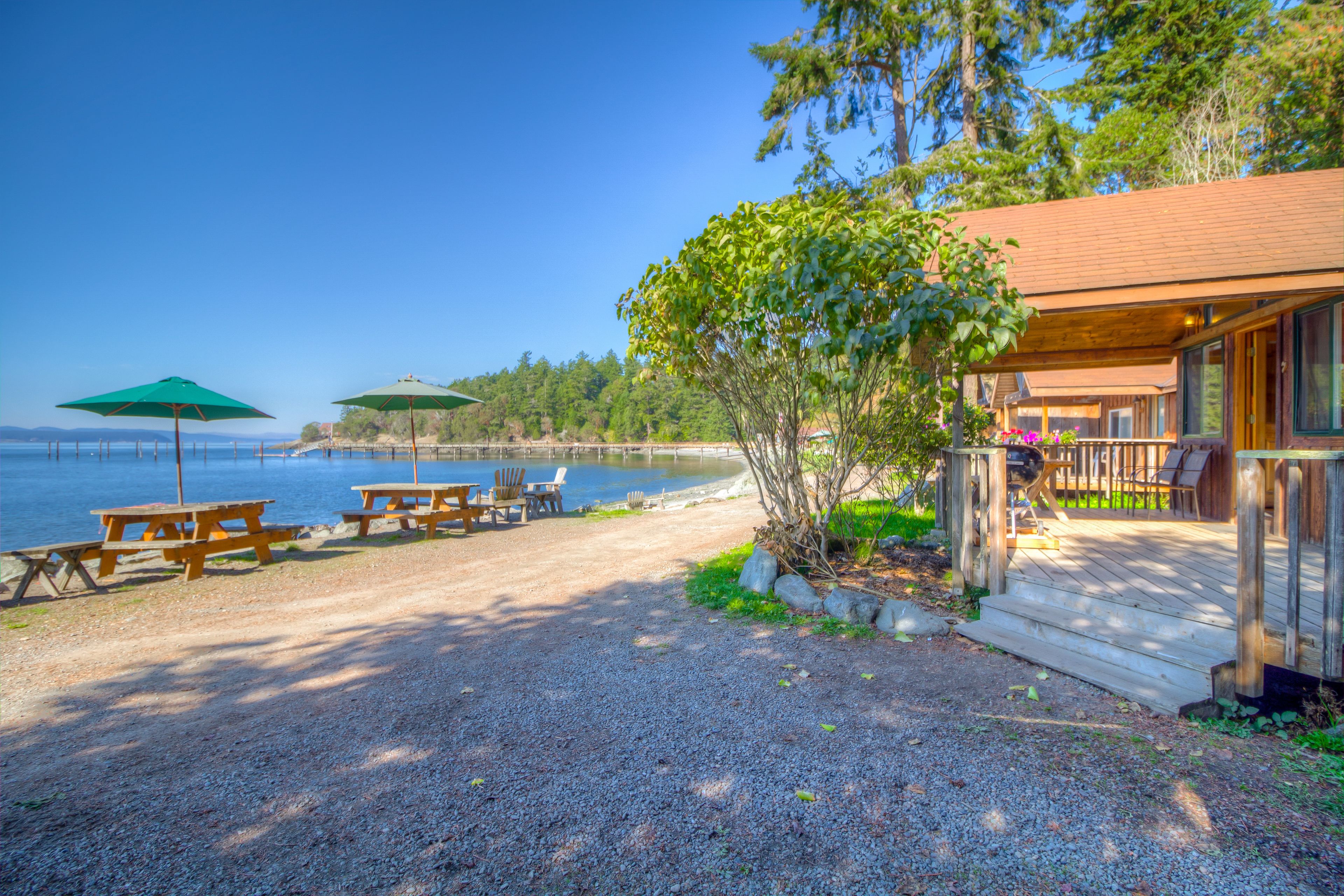 A lakeside cabin with picnic tables and umbrellas, a deck, and a view of the lake.