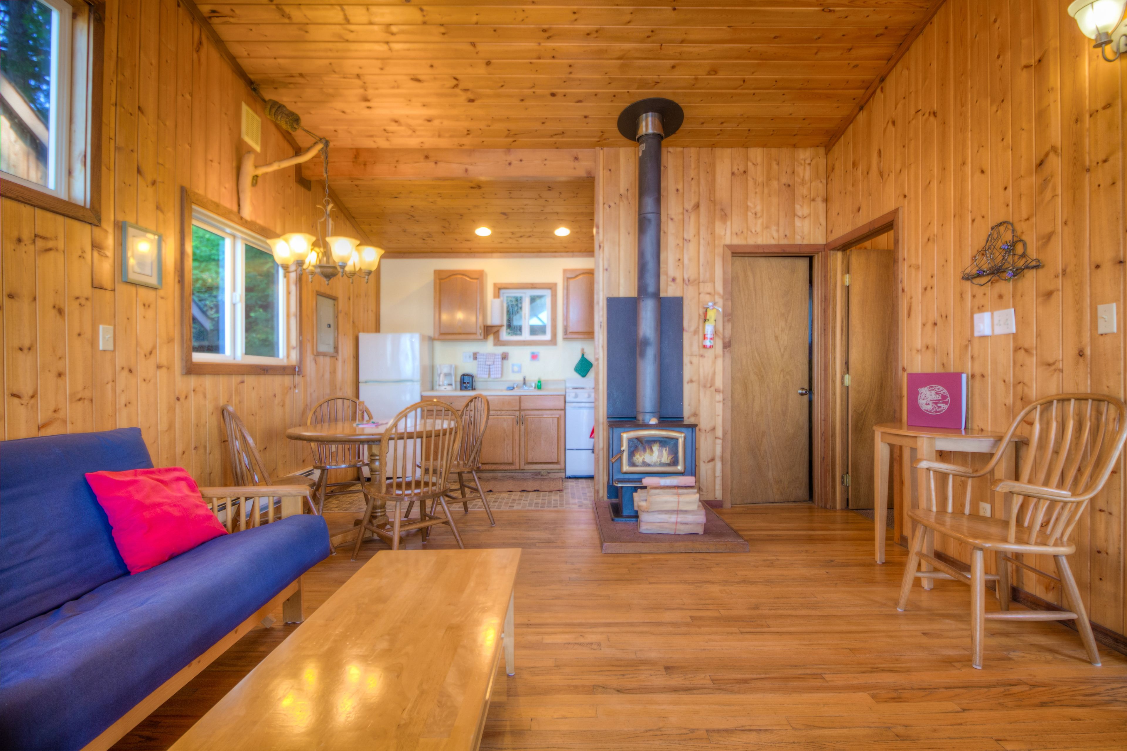 A cozy cabin interior with a wooden interior, a sofa, a dining table, and a kitchen area with a wood stove.