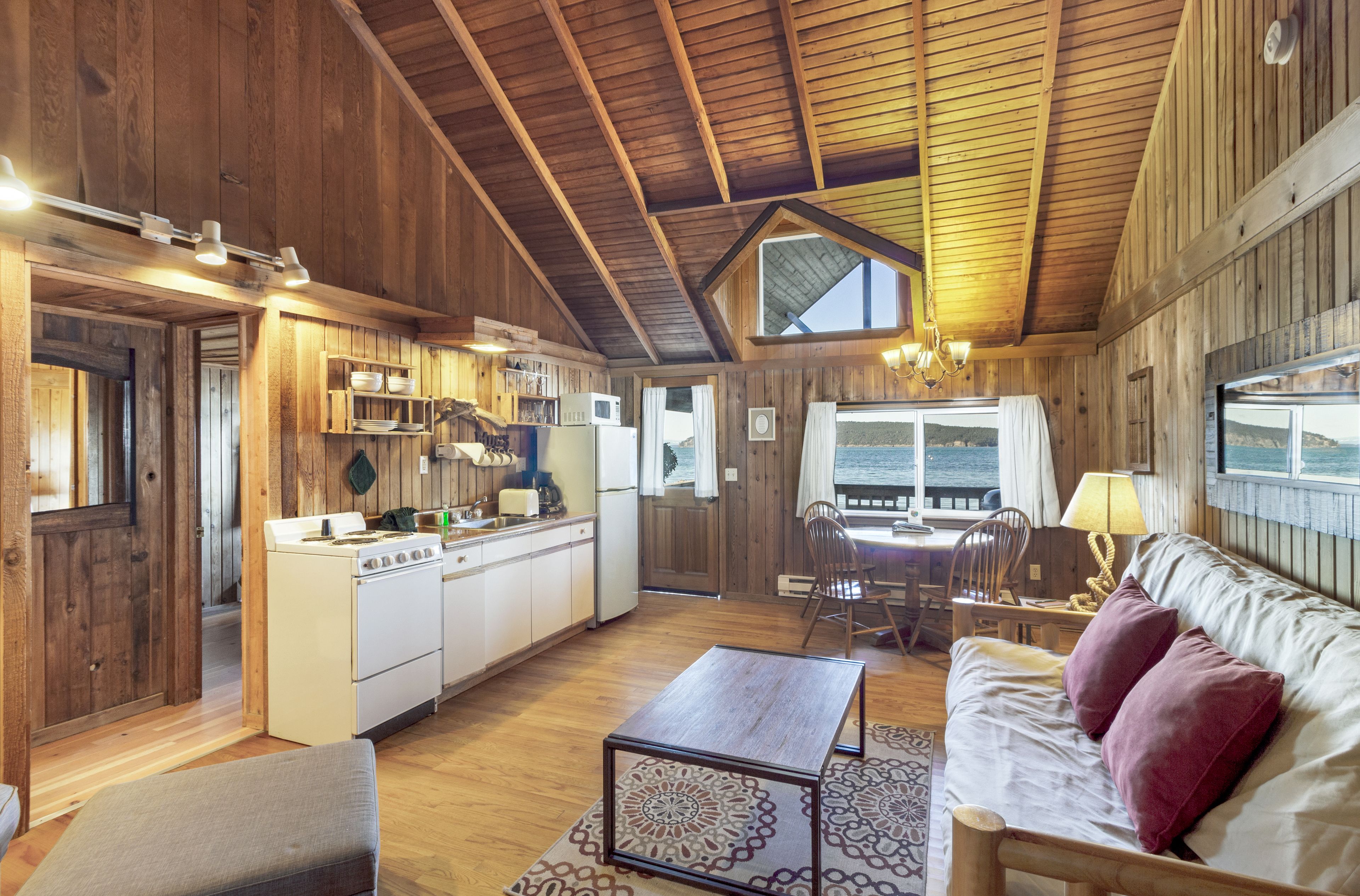 A cozy cabin interior with a kitchen, dining area, and a large window overlooking the ocean.