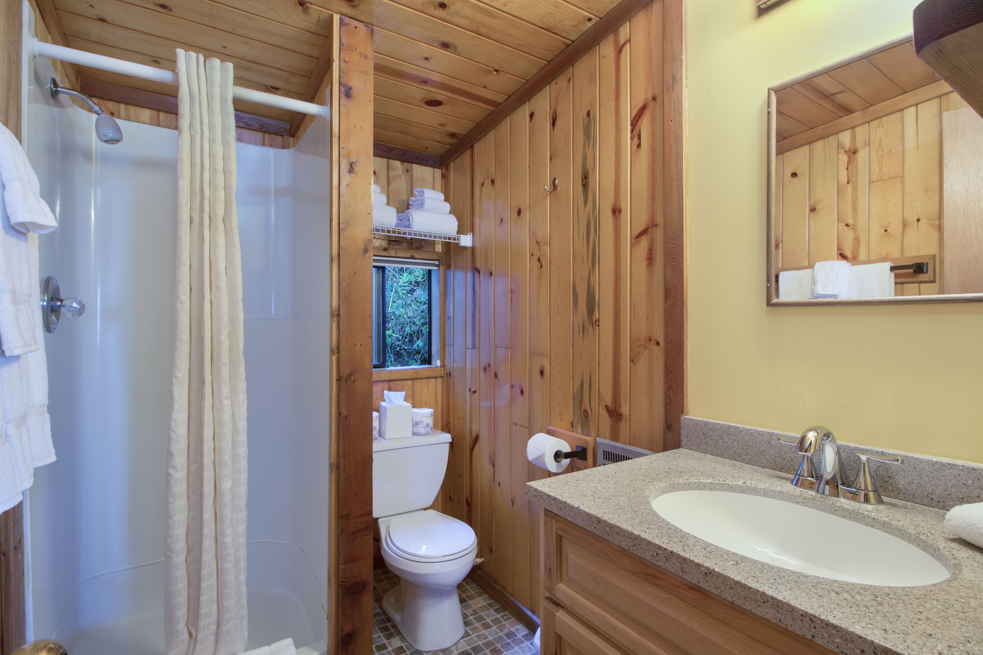 Un baño de madera con ducha, inodoro y lavamanos.