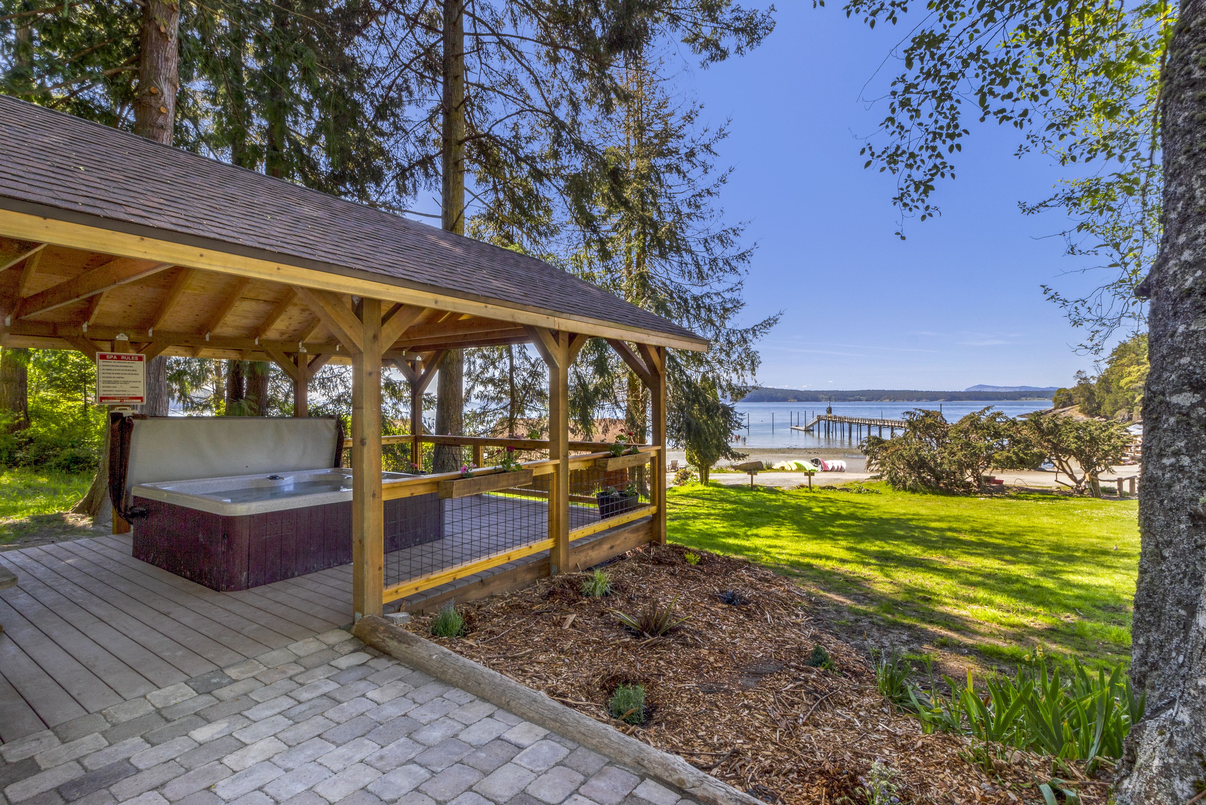 Une terrasse en bois avec un jacuzzi, un espace salon couvert et une vue sur l’eau.