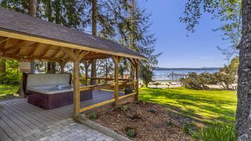 Une terrasse en bois avec un jacuzzi, un espace salon couvert et une vue sur l’eau.