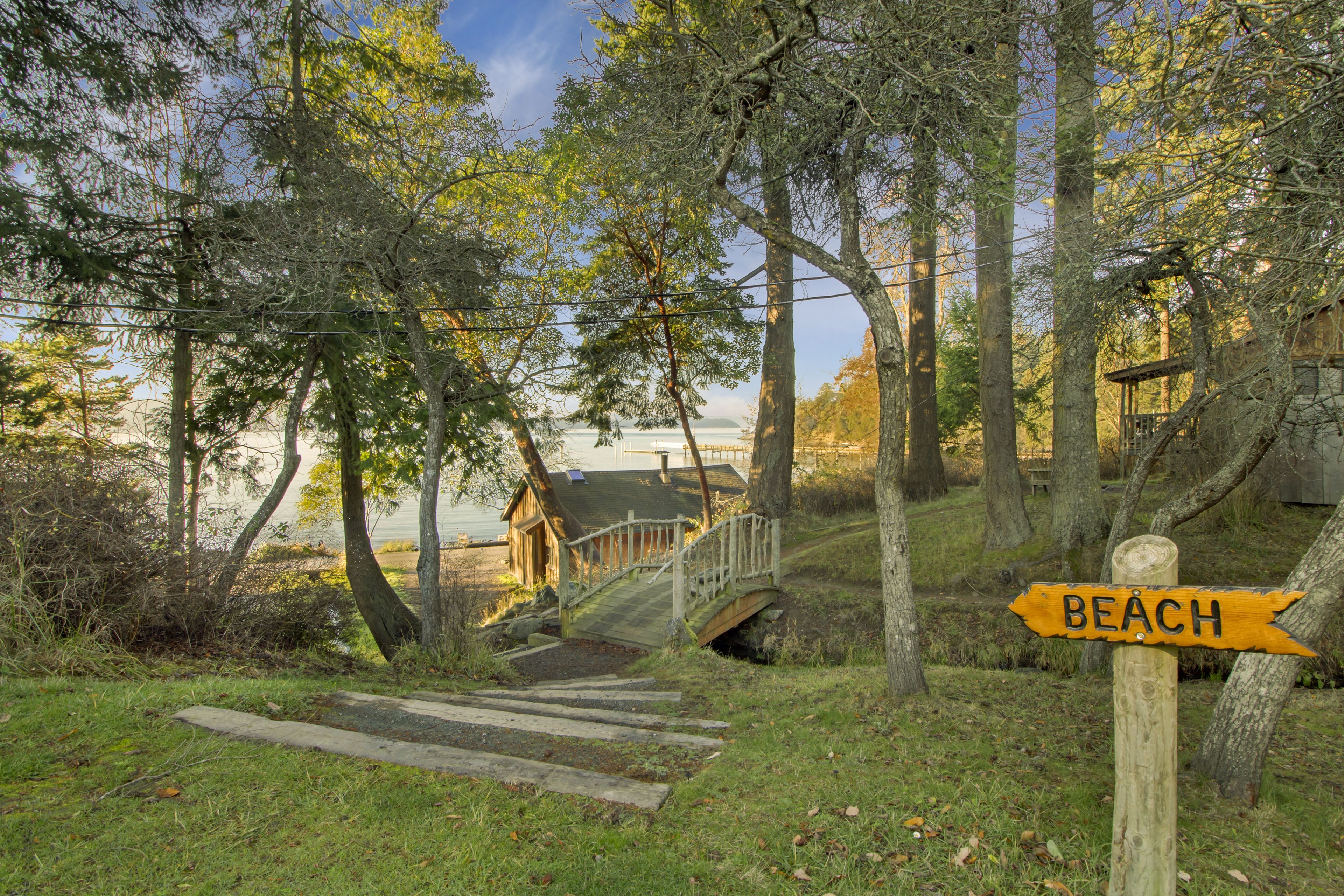 A wooden bridge leading to a beach, surrounded by trees and a wooden cabin.