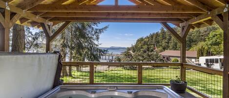 Un jacuzzi bajo un porche de madera con vista a un lago y un bosque.