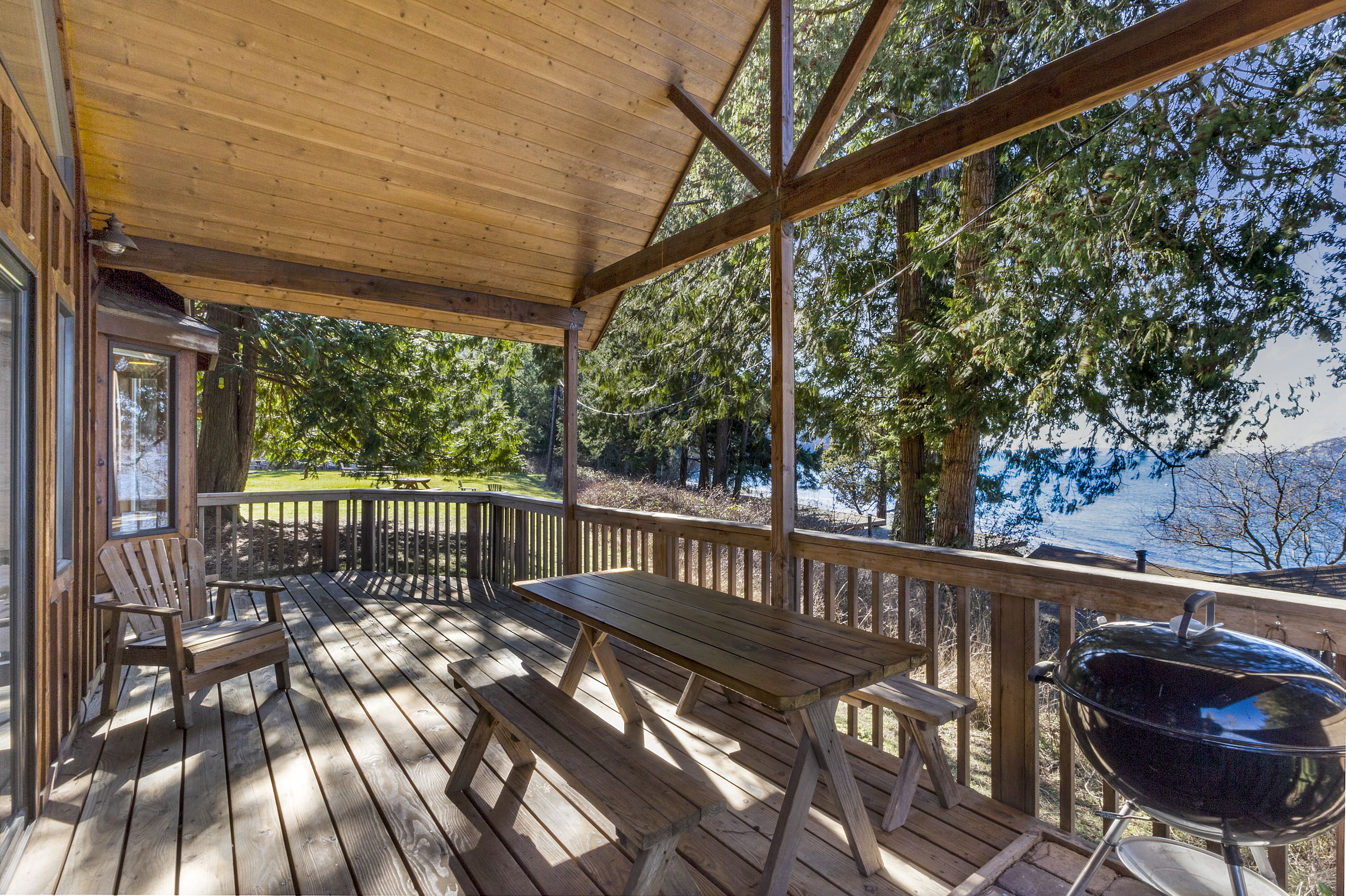 Une terrasse en bois avec une table de pique-nique et des chaises, un barbecue et une vue sur un lac.
