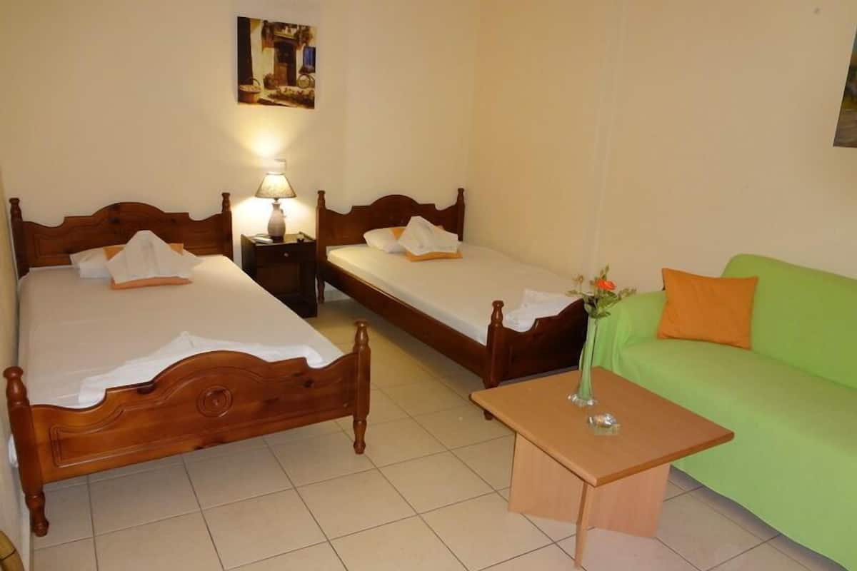 A room with two wooden beds, a green sofa, and a small wooden table with a vase.